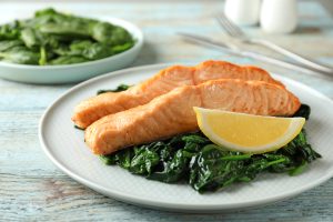 Cooked salmon with spinach and lemon on wooden table, closeup. These are all foods that can combat dry eye symptoms!