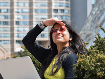 Person with black hair looking upward and wearing sunglasses with rose-tinted lenses to protect their eyes this summer.