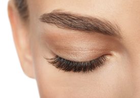 Close-up photo of a model wearing eye makeup closed eyes and long eyelashes.
